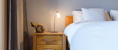 Una camera da letto con un comodino in legno, una lampada, un pesce decorativo e un letto con biancheria bianca.