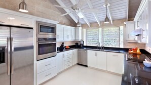 A modern kitchen with stainless steel appliances, white cabinetry, and a ceiling fan. - Tropical Oasis with Pool Near Beach - Todmorden (Gibbes Beach)