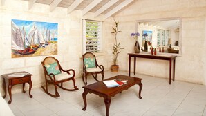 A room with a wooden coffee table, two rocking chairs, a potted plant, a painting of sailboats, and a large mirror. - Tropical Oasis with Pool Near Beach - Todmorden (Gibbes Beach)