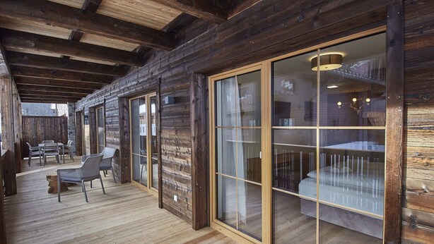 Un intérieur en bois avec un plafond haut, une porte-fenêtre coulissante donnant sur un balcon et un coin salon avec des fauteuils.