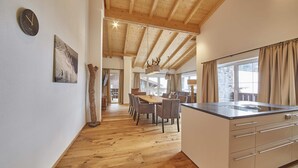 Une cuisine moderne avec un plafond en bois, un coin repas avec une table et des chaises en bois, et une vue sur l’extérieur grâce à de grandes fenêtres.