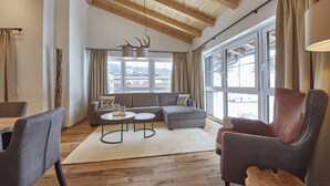Un salon moderne avec un plafond en bois, de grandes fenêtres, un canapé gris, une table basse ronde et un fauteuil en cuir.