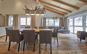 A spacious dining area with a wooden table and chairs, large windows, and a high ceiling with exposed beams. - Residenz Der Wieshofer (Saalbach-Hinterglemm)