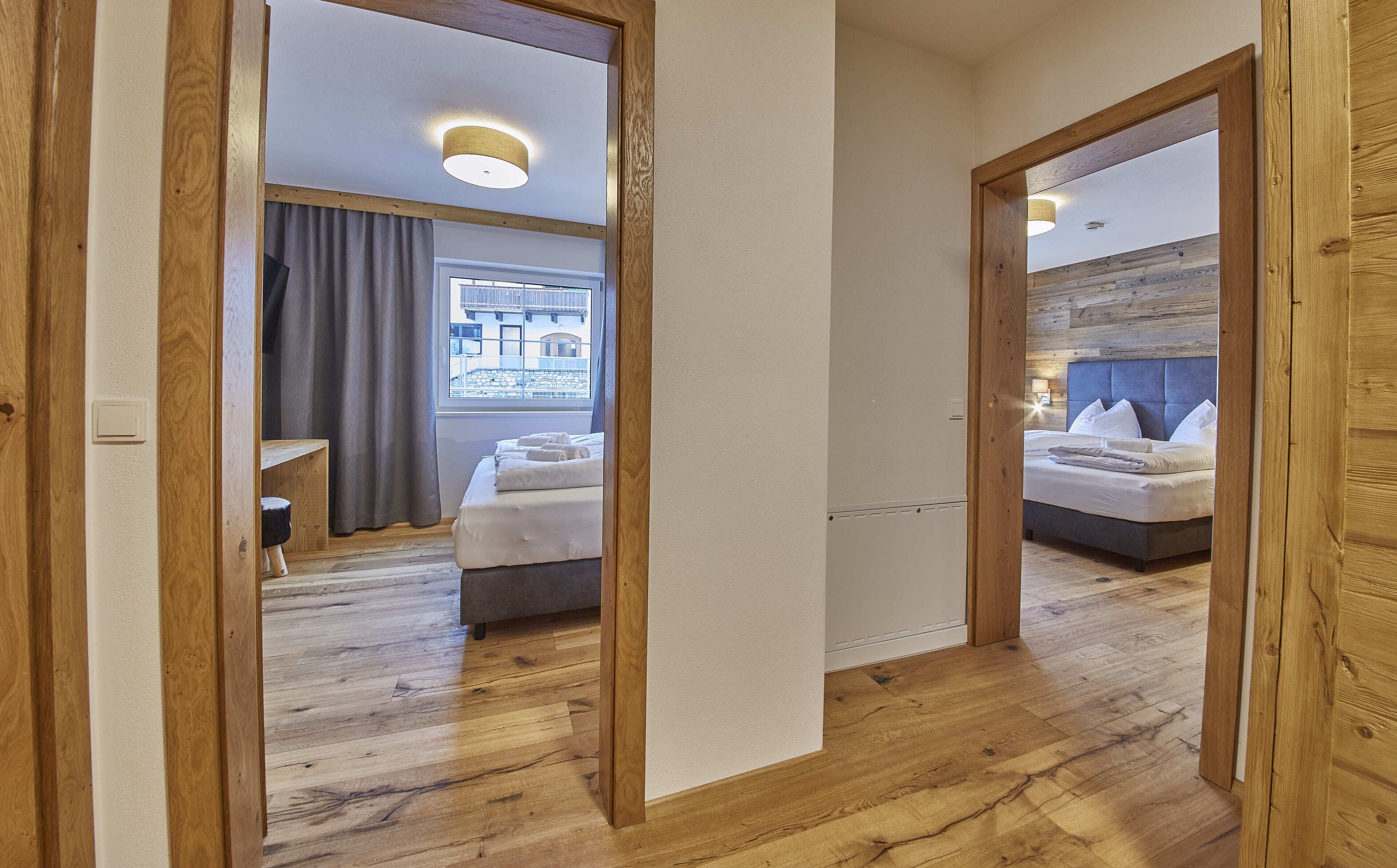 A hotel room with a wooden floor, a bed with white linens, a bedside table, and a window with curtains.
