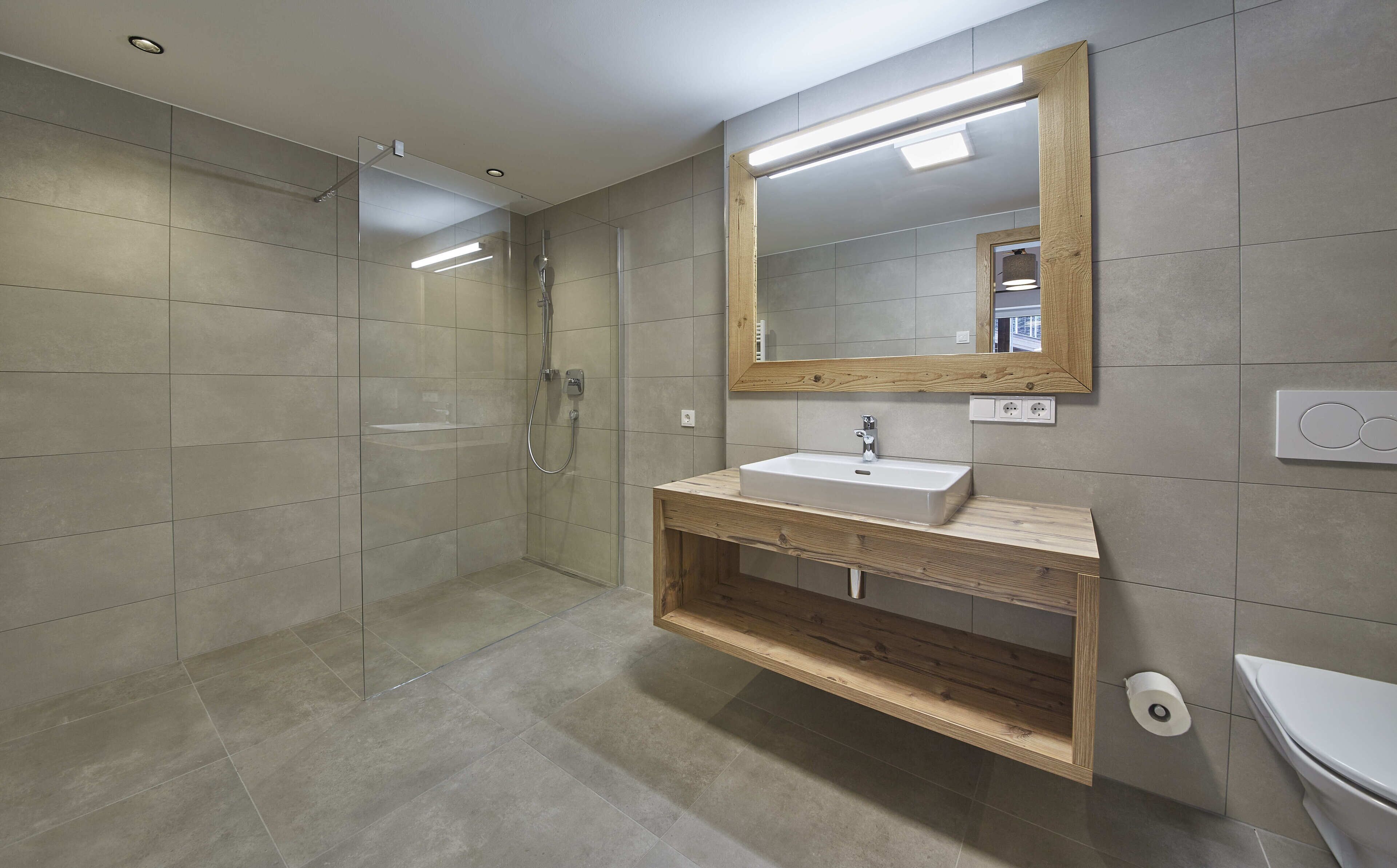A modern bathroom with a glass shower enclosure, a wooden vanity with a sink, and a large mirror.