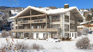 Un grand immeuble à étages, doté d’une façade en pierre et de balcons en bois, entouré d’un paysage enneigé.