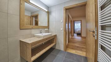 Une salle de bain moderne avec un meuble-lavabo en bois, un grand miroir et une vue sur une chambre à coucher, grâce à une porte ouverte.