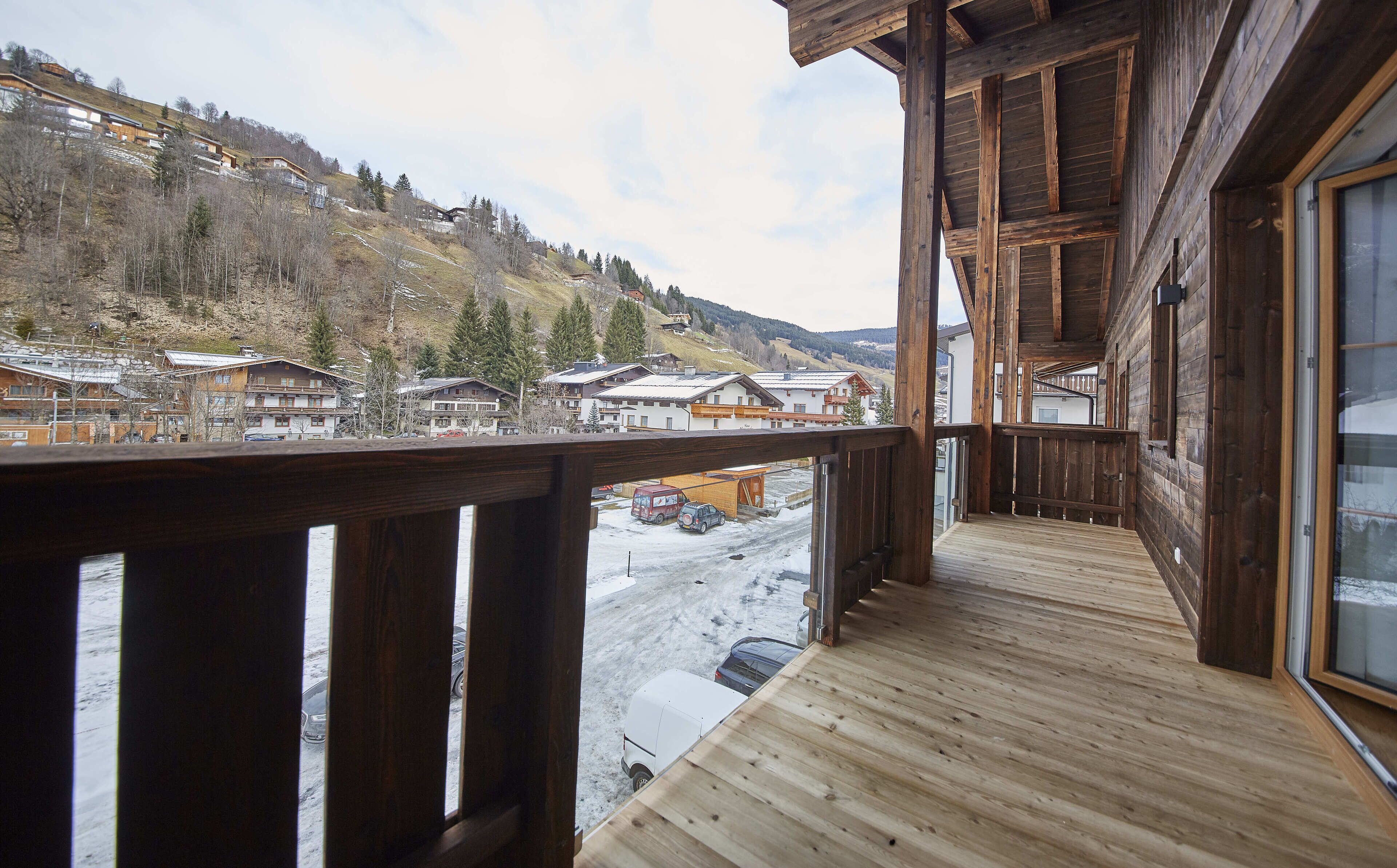 A wooden balcony with a view of a snowy village and mountains.