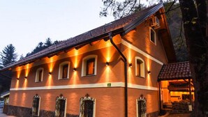 A building with a sloped roof, multiple windows with decorative iron grilles, and a stone base. - Guesthouse Gorska Reka (Zrece)