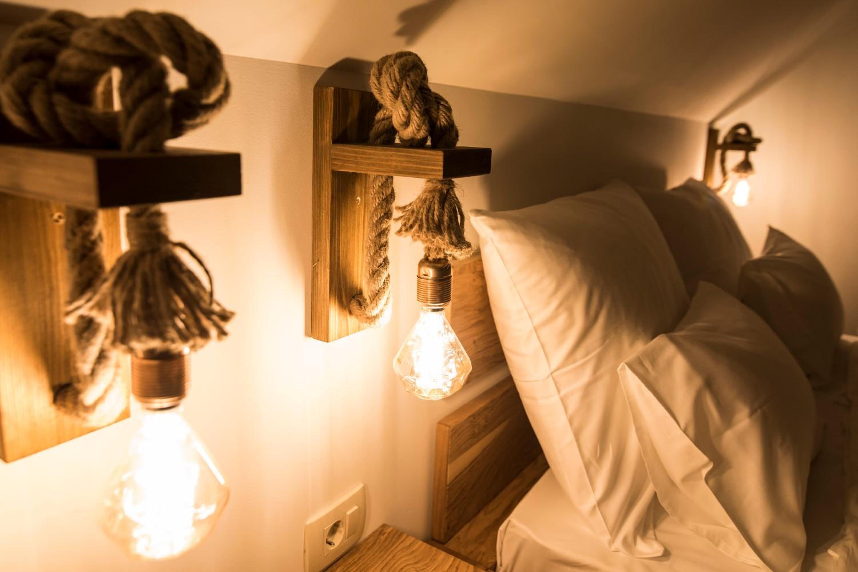 A bedroom with a bed, white pillows, and two wall-mounted light fixtures with exposed bulbs.
