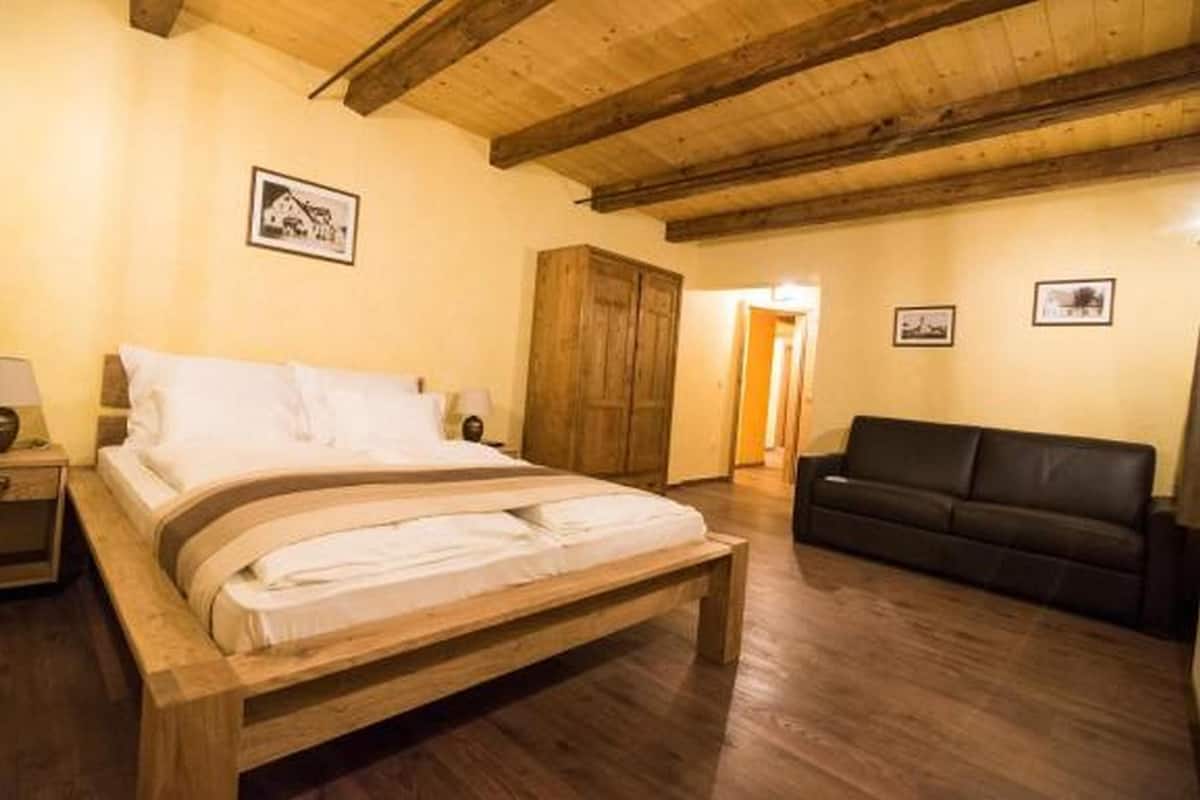 A bedroom with a wooden bed, a black leather sofa, wooden walls, and a wooden ceiling.
