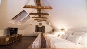 A bedroom with a sloped ceiling, a bed with white bedding, a wooden headboard, a TV on a wooden stand, and a small window. - Guesthouse Gorska Reka (Zrece)