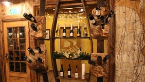 A wooden wine rack with bottles and glasses, a door with a window, and a sign with a logo. - Guesthouse Gorska Reka (Zrece)