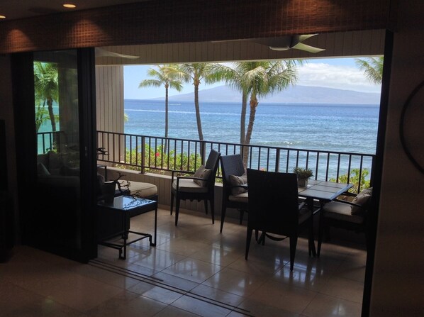 A balcony with a view of the ocean, a table, and chairs.