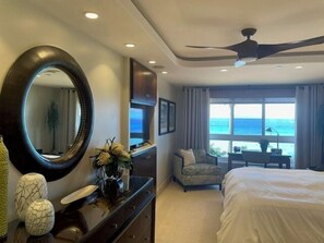 A hotel room with a bed, a desk, a chair, a large mirror, and a view of the ocean.