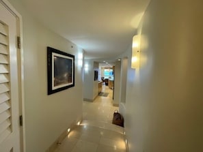 A hallway with a framed picture on the wall, a door on the left, and a bag on the floor.