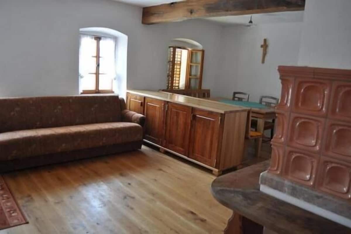 A room with a wooden sofa, a kitchen area with a wooden countertop, and a stone fireplace.