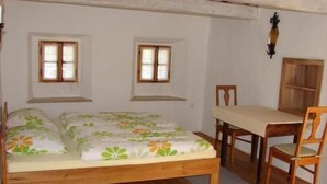 Um quarto pequeno e acolhedor com uma cama de solteiro, uma mesa de madeira e duas janelas.