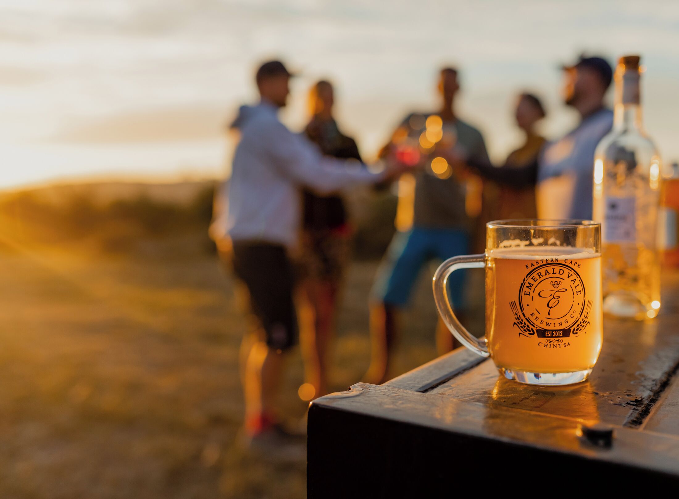 A group of people at a beach with a beer mug on a table.
