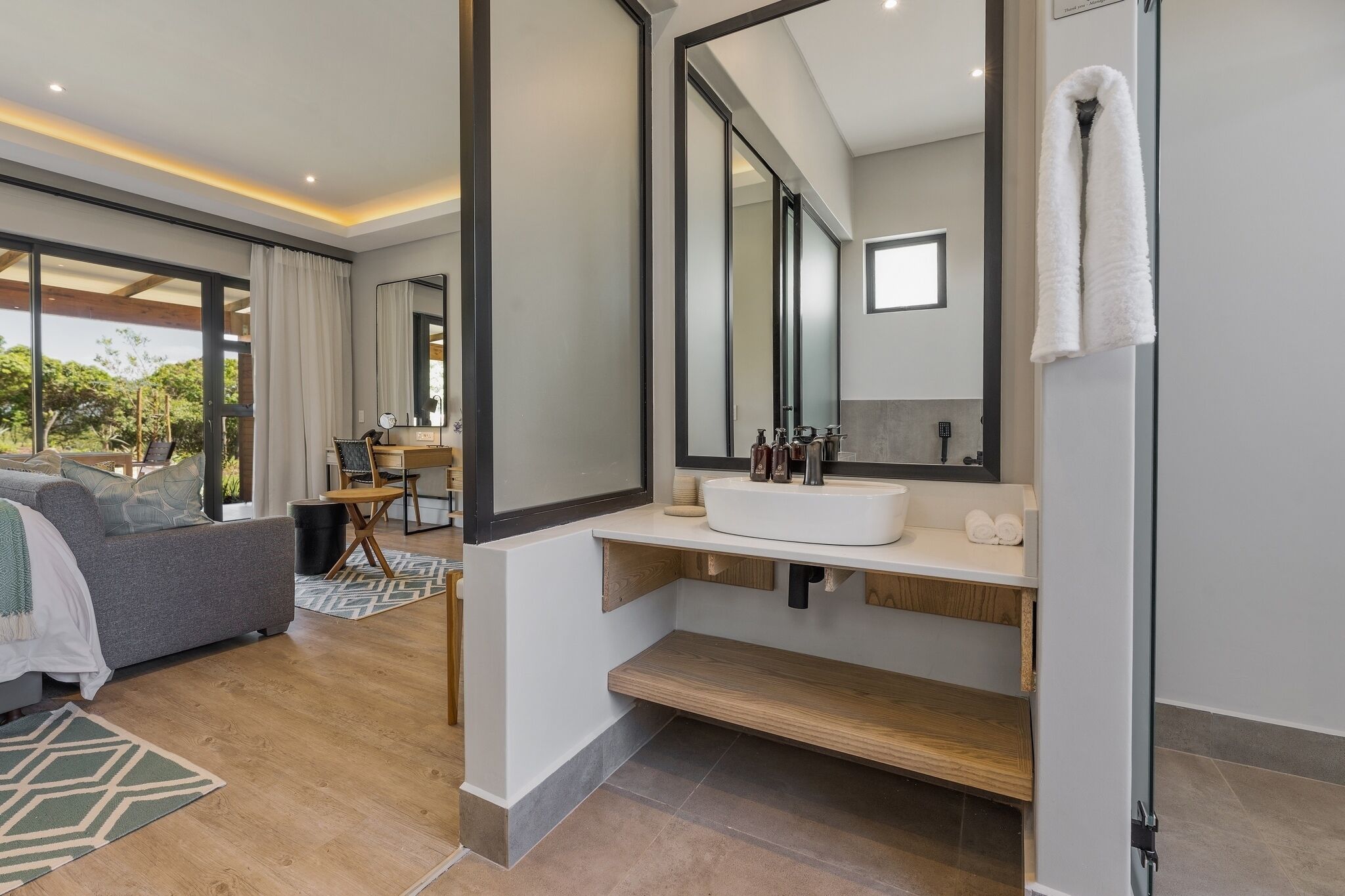 A modern bathroom with a large mirror, white sink, and wooden shelves.