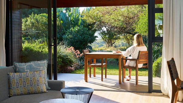 A modern outdoor seating area with a wooden table and chairs, a cushioned sofa, and a small round table. - Hotel Olivewood (Great Kei)