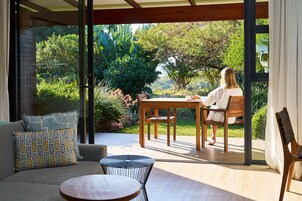 Un espacio exterior moderno con zona de estar, mesa de madera y sillas, un sofá acolchado y una pequeña mesa redonda.