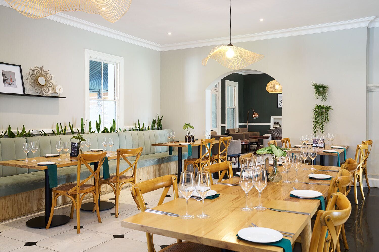 A dining area with wooden tables and chairs, a green sofa, and a large window.