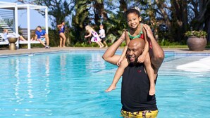 A man carrying a child on his shoulders by a poolside. - Hotel Olivewood (Great Kei)