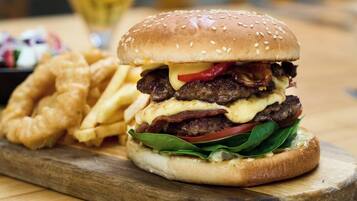Una hamburguesa con papas fritas sobre una tabla de madera, una jarra de cerveza y una silla al fondo.