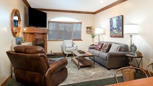 A cozy living room with a leather recliner, a gray sofa, a wooden coffee table, and a fireplace.