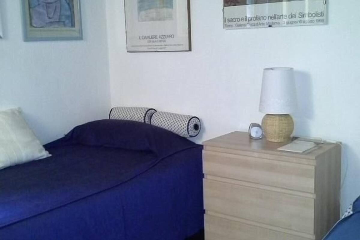 Un dormitorio con una cama individual, una mesita de noche, una lámpara y dos cuadros enmarcados en la pared.