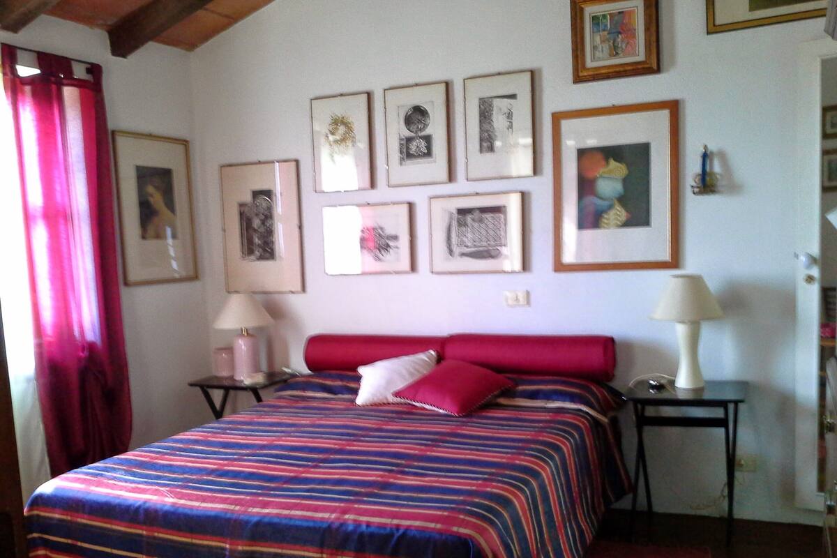 Un dormitorio con cama, dos mesitas de noche, una lámpara y varias fotografías enmarcadas en la pared.