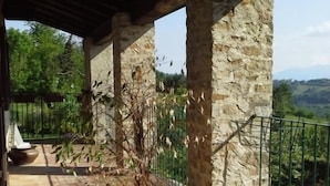 A covered outdoor area with stone pillars, a potted plant, a bench, and a view of the landscape. - Villa Malgrè Tout (Bonvicino)