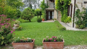 A stone building with a green door, surrounded by a well-maintained garden with various plants and flowers. - Villa Malgrè Tout (Bonvicino)