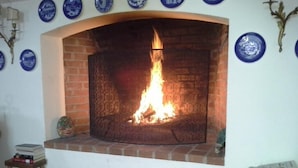 A fireplace with a fire, a small table with books, and decorative plates on the wall. - Villa Malgrè Tout (Bonvicino)