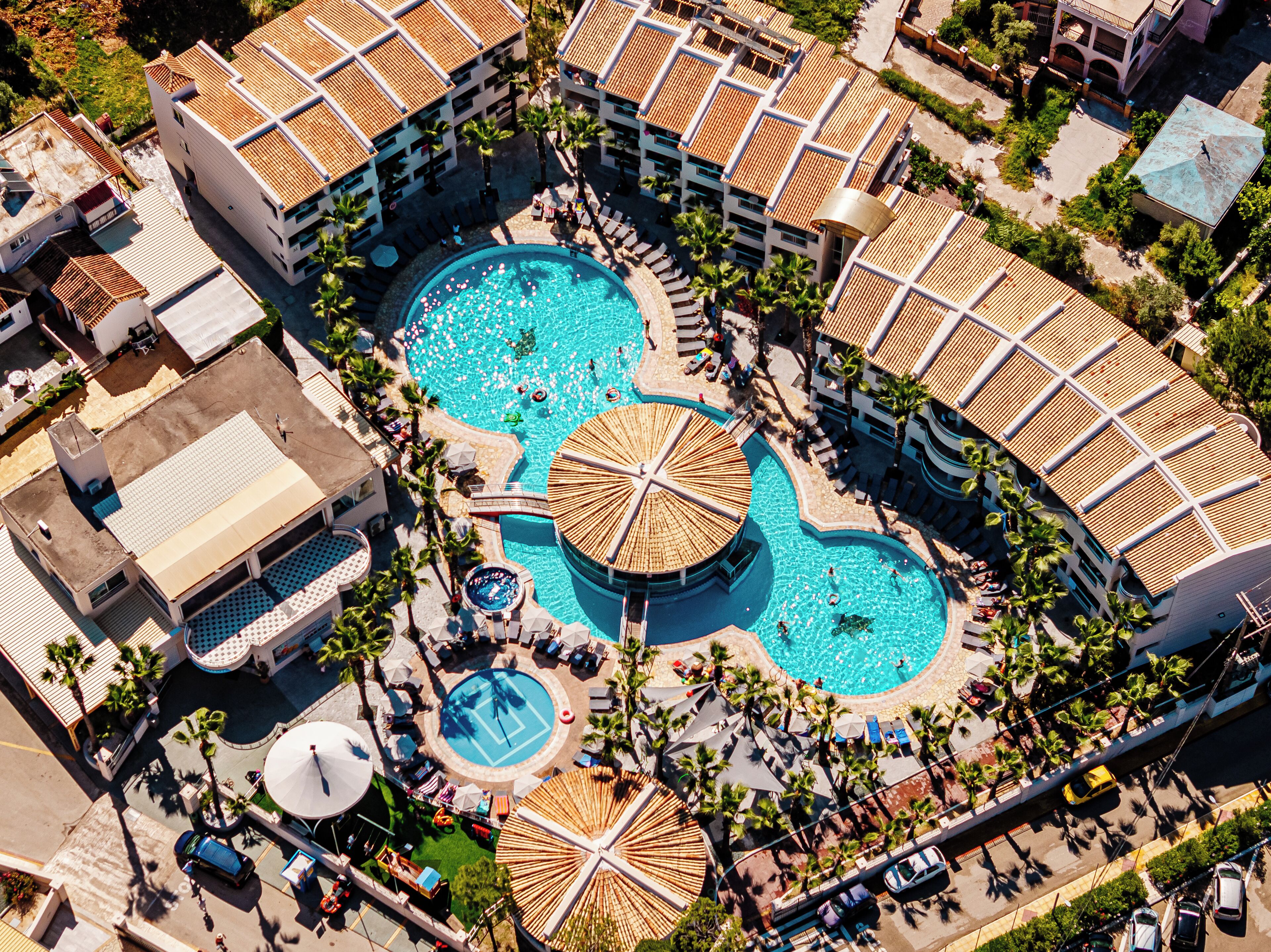 An aerial view of a resort with multiple swimming pools, sun umbrellas, and lounge areas.