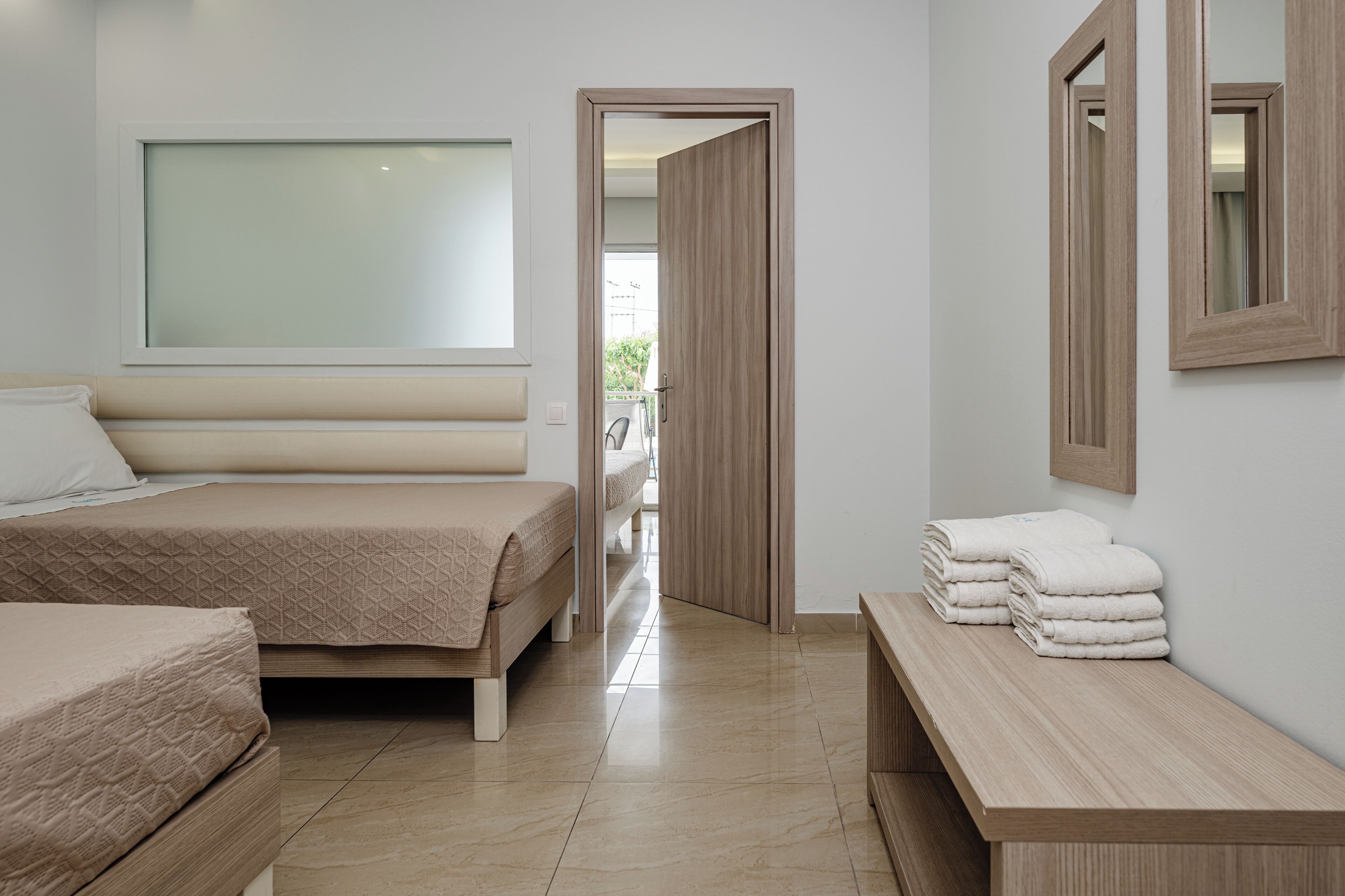 Un dormitorio moderno con una cama grande, un banco con toallas y un espejo en la pared.