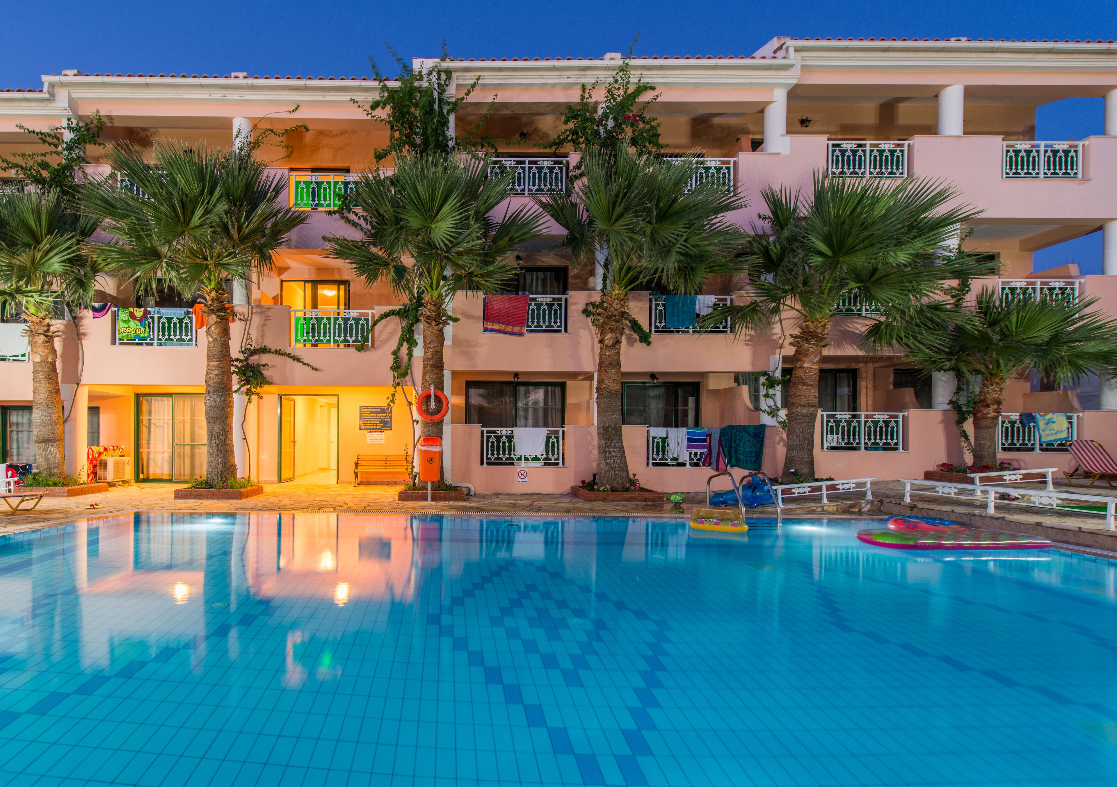 A hotel with a swimming pool, palm trees, and balconies with railings.