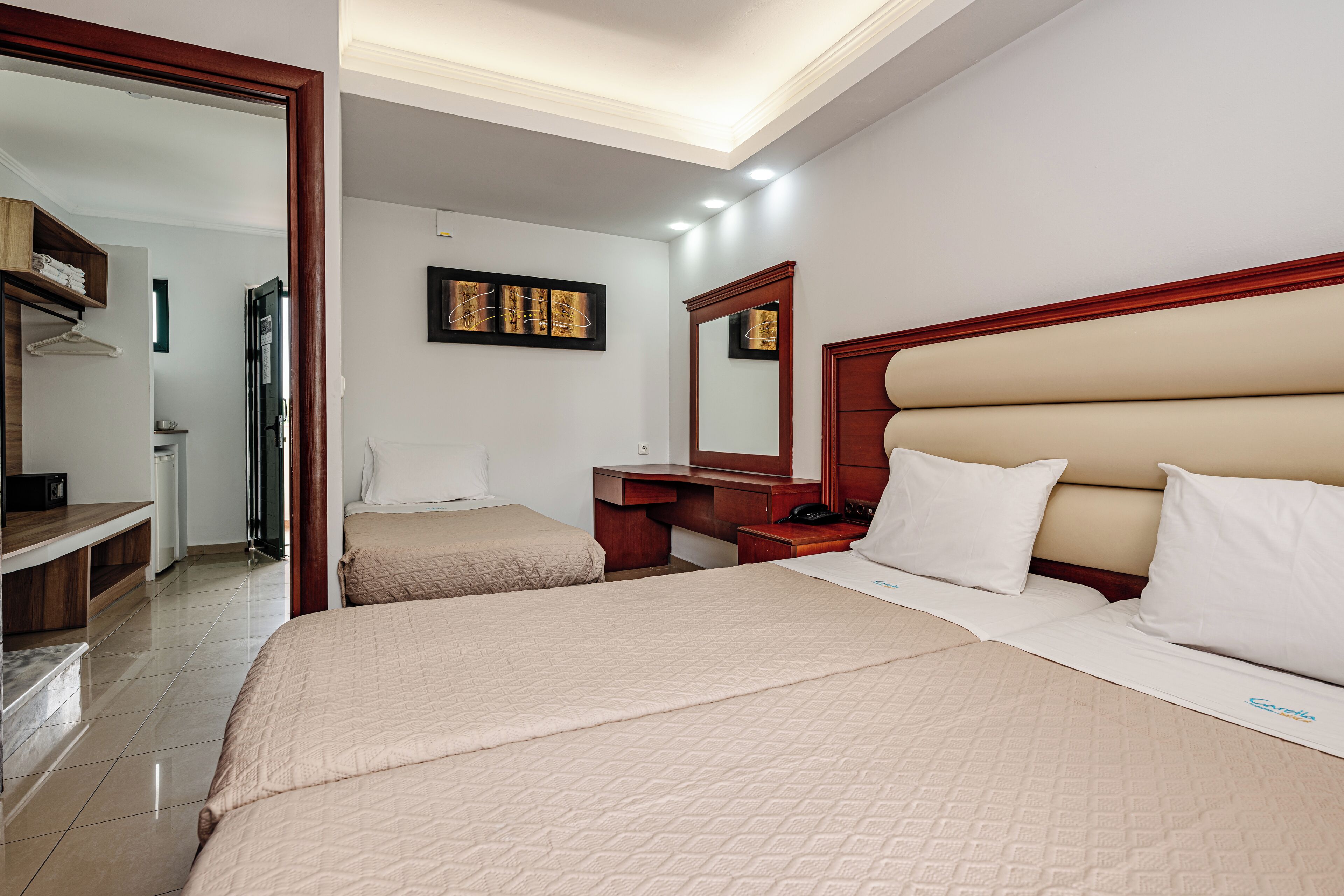 A hotel room with two beds, a wooden headboard, a bedside table, a mirror, and a wall-mounted artwork.