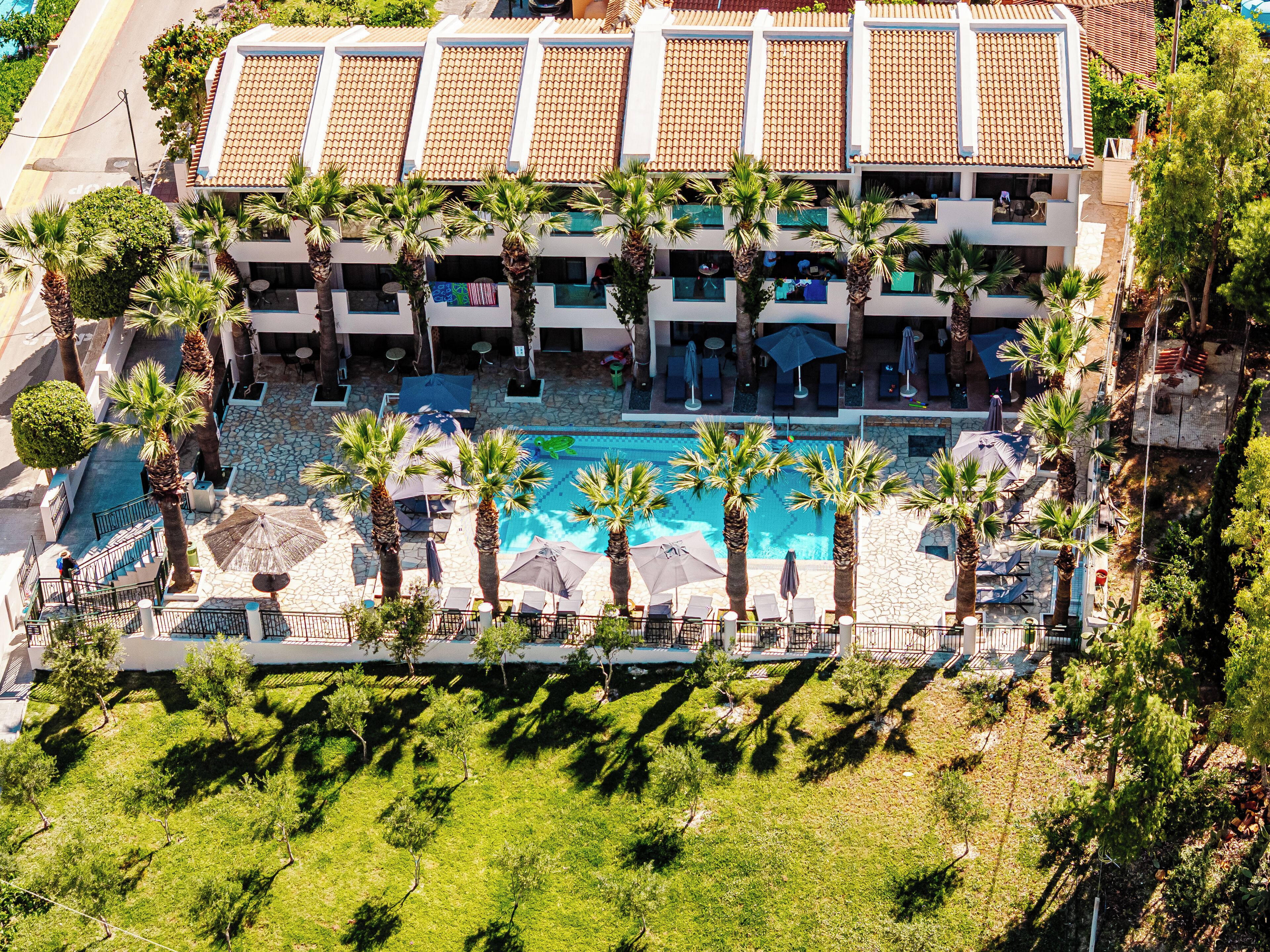 Un hotel de varios pisos con piscina rodeada de palmeras y sillas de descanso.