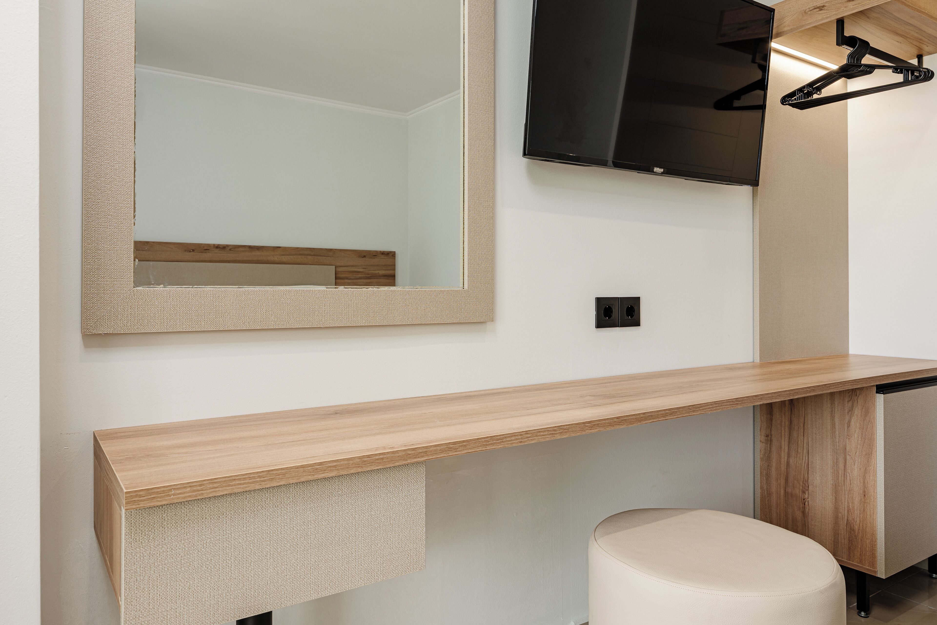 A modern bathroom with a wooden vanity, a mirror, a toilet, and a wall-mounted TV.
