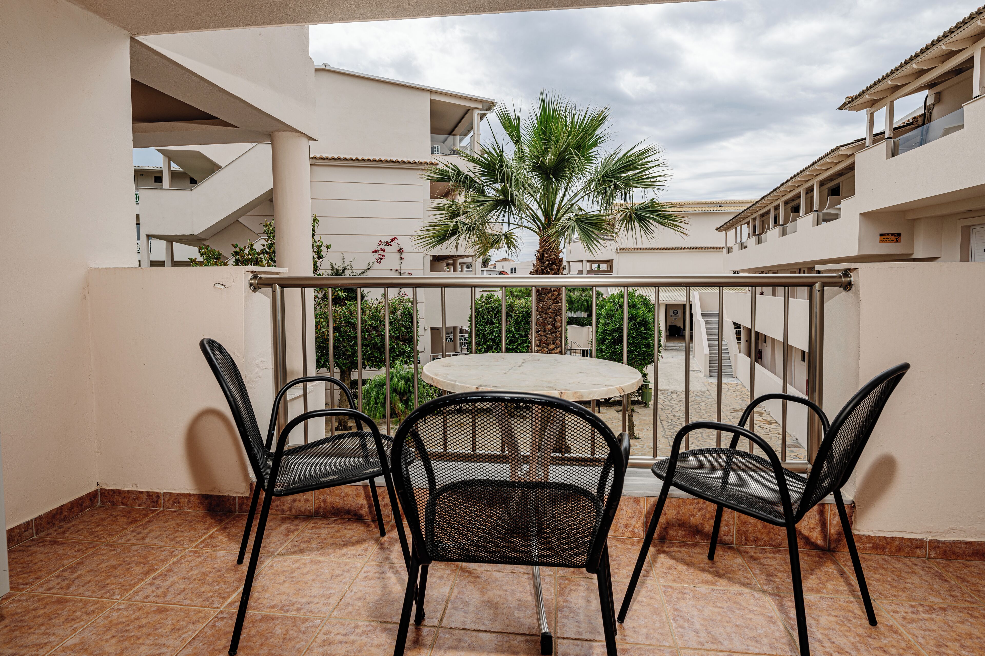 Un balcone con un tavolo rotondo e quattro sedie, una palma e vista su un edificio con balconi.