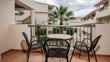 Un balcone con un tavolo rotondo e quattro sedie, una palma e vista su un edificio con balconi.