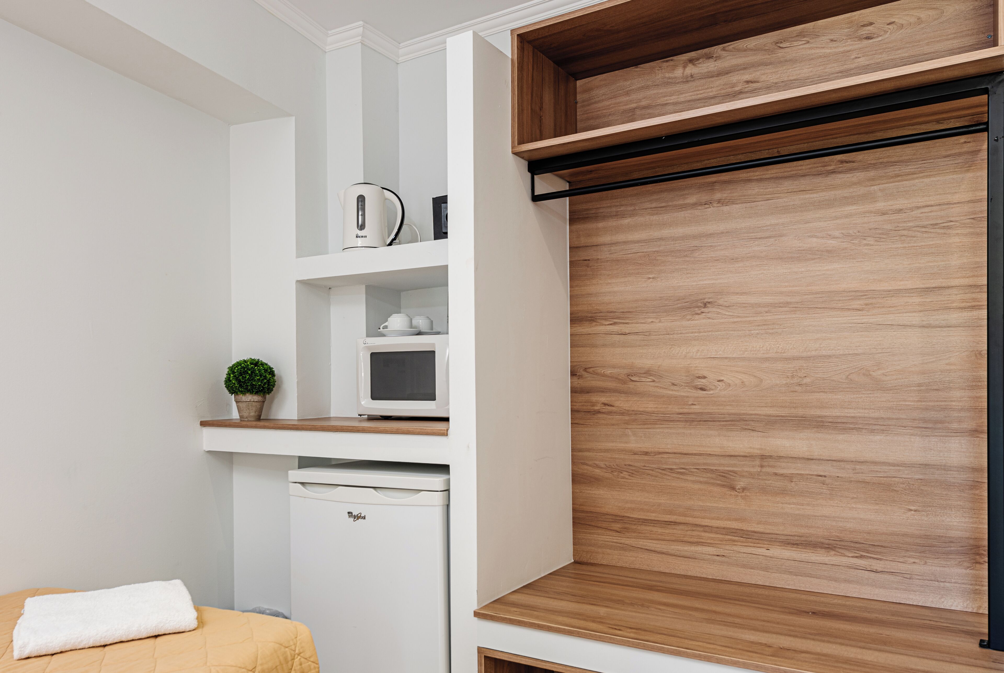 A compact kitchenette with a microwave, kettle, and a small potted plant.