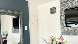 A modern dining area with a large mirror, a table with chairs, a vase of flowers, and a television mounted on the wall. - Guesthouse Vladimir & Ana (Pancevo)