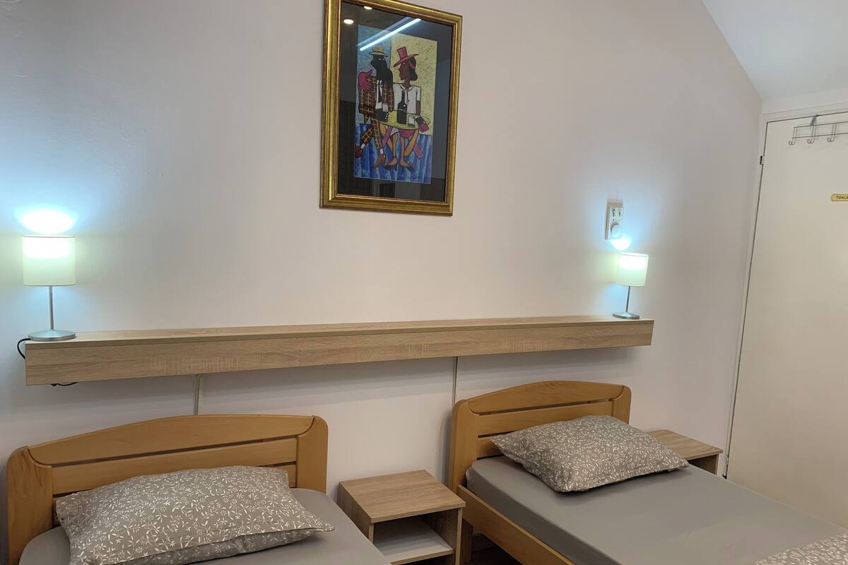 Un dormitorio con dos camas individuales, cabeceros de madera, una mesita de noche y una repisa sobre las camas, además de un cuadro enmarcado en la pared.