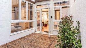 Une terrasse en bois avec un mur extérieur peint en blanc et de grandes fenêtres.