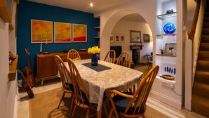A dining area with a table set for six, surrounded by wooden chairs. There is a vase with yellow flowers on the table, and a guitar is leaning against the wall. - 3 bedroom  family friendly and pet friendly cottage in Narberth, Pembrokeshire (Narberth)