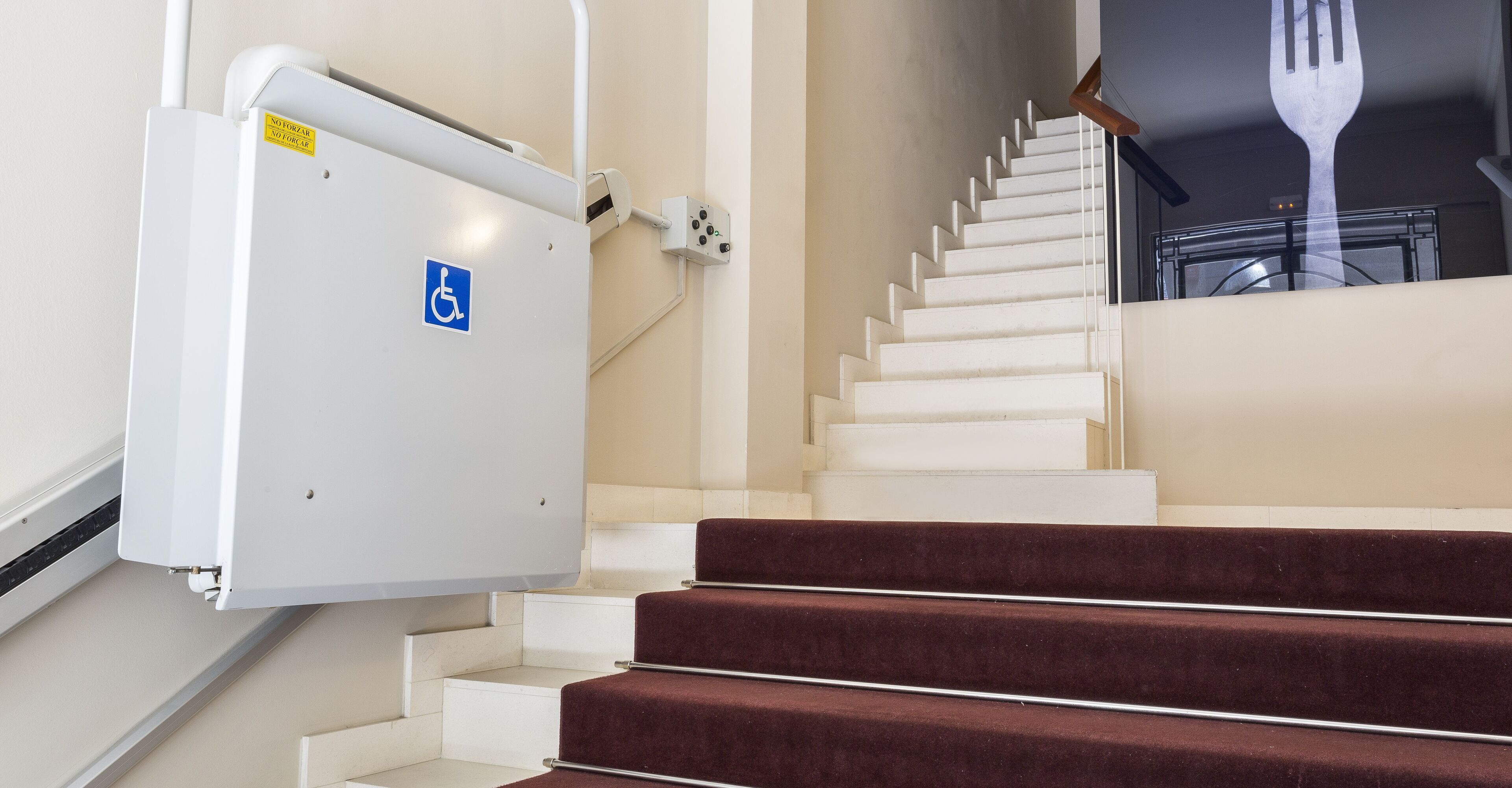A staircase with a handrail, a disabled access sign, and a fork leaning against the wall.