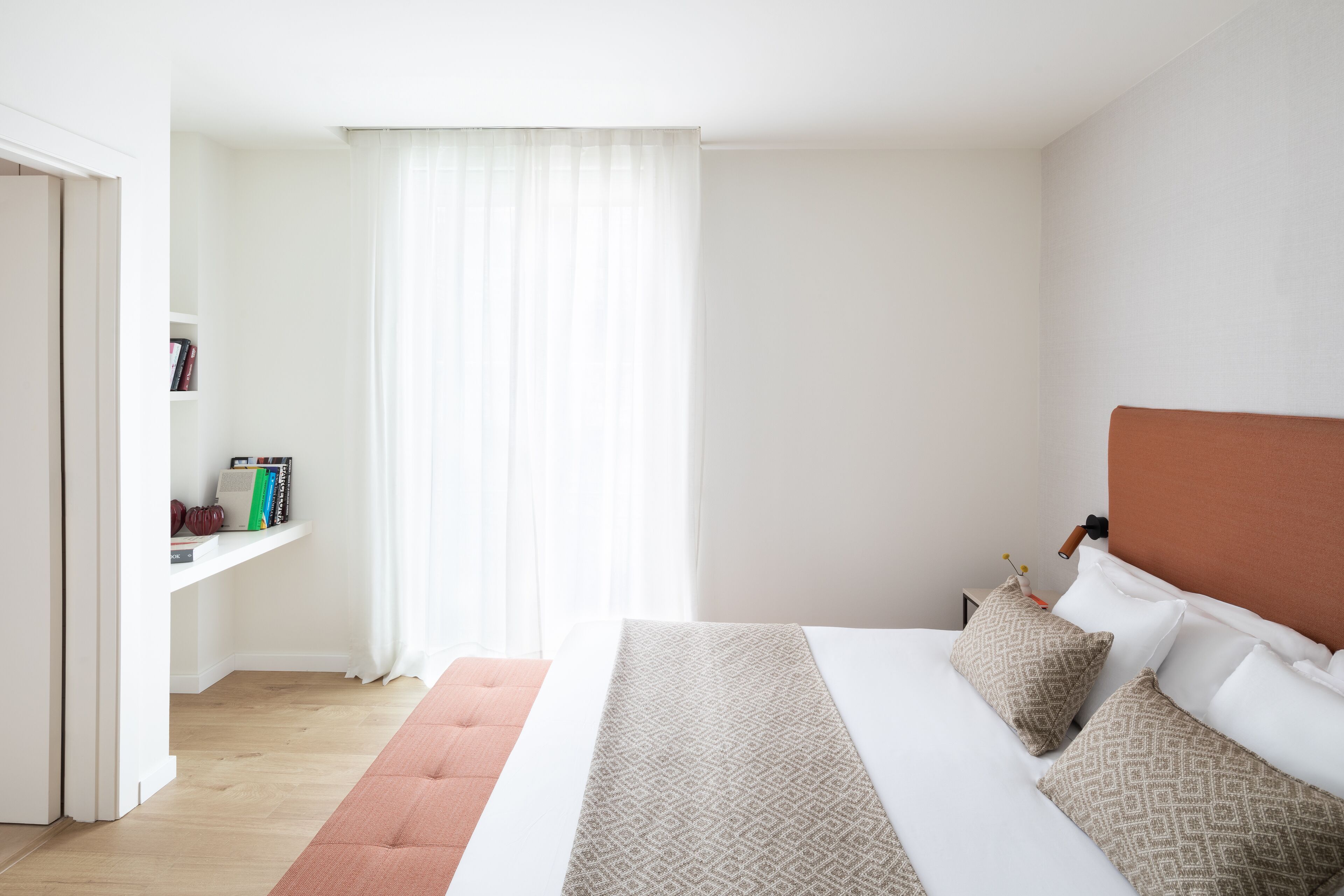 A bedroom with a bed, a nightstand, a bookshelf, and a window with curtains.